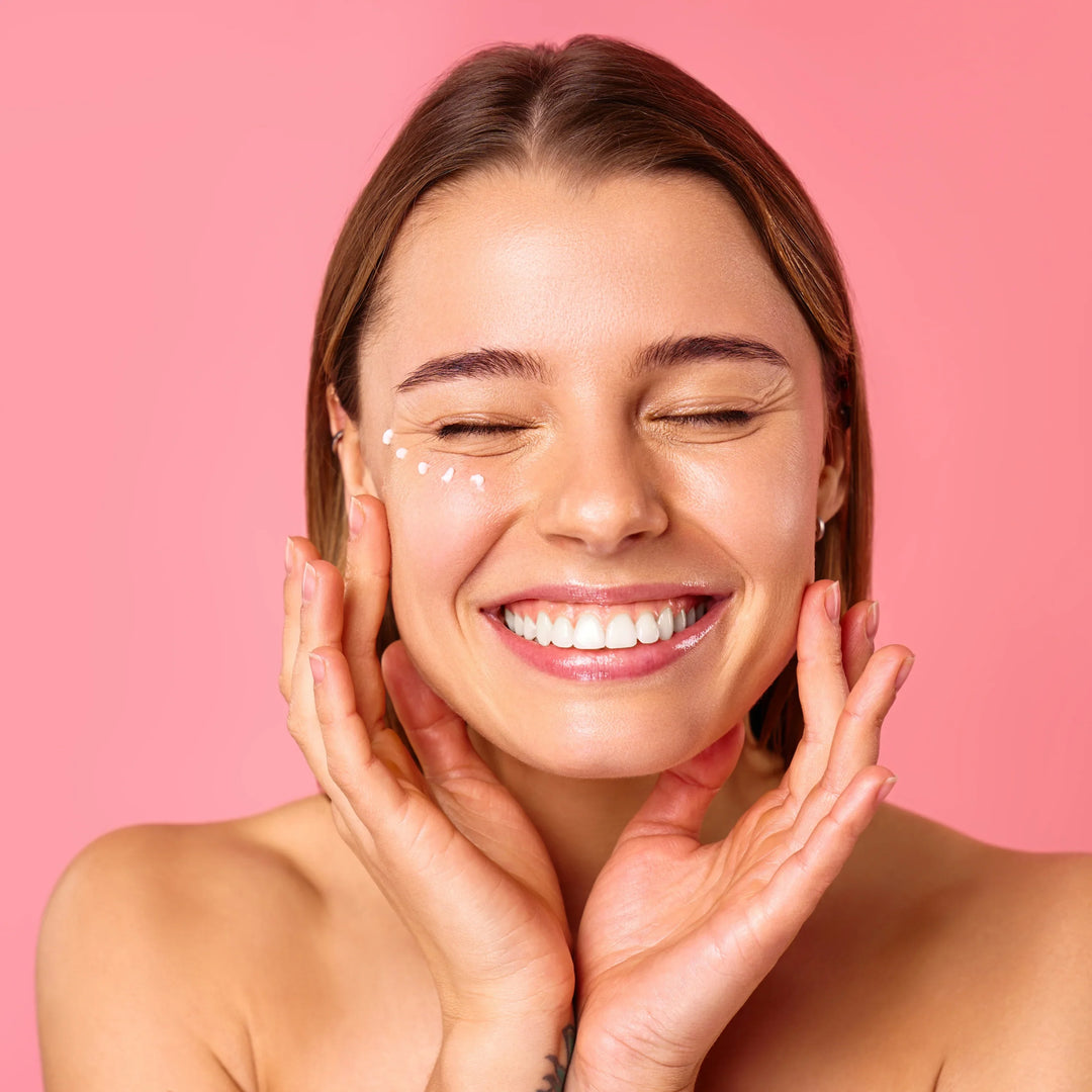 Una donna applica una crema contorno occhi, con lo sfondo sfocato di un bagno luminoso.